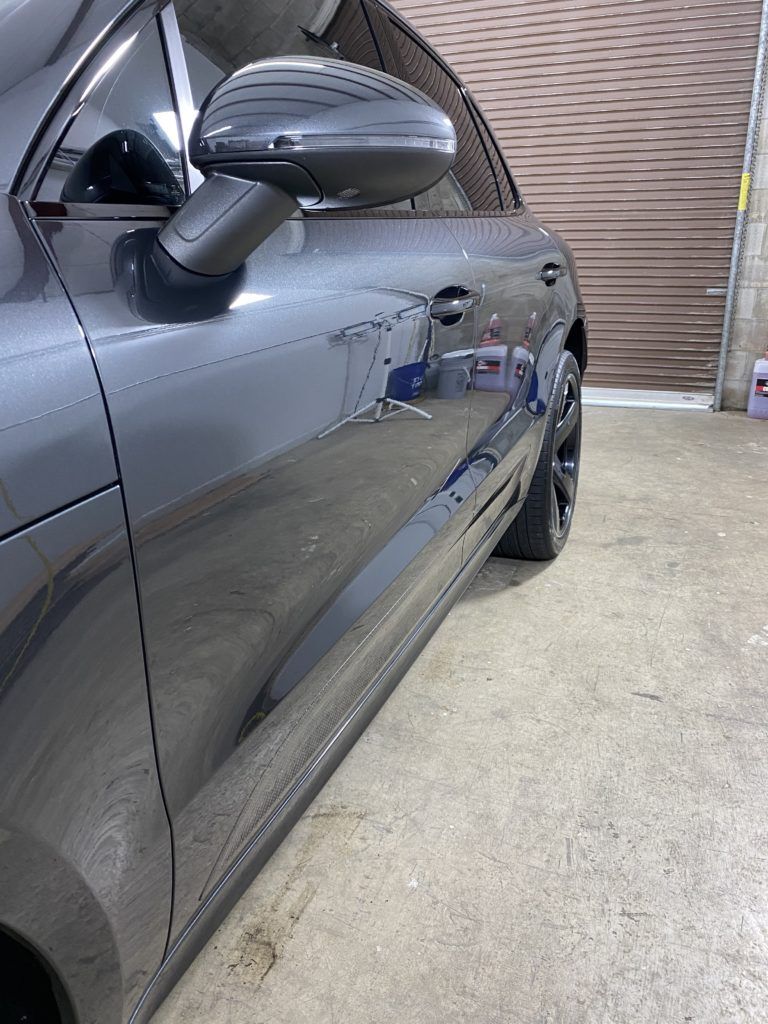 A gray car is parked in a garage next to a garage door.