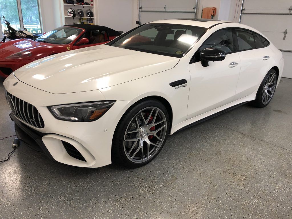 A white mercedes amg gt 63 s is parked in a garage next to a red sports car.