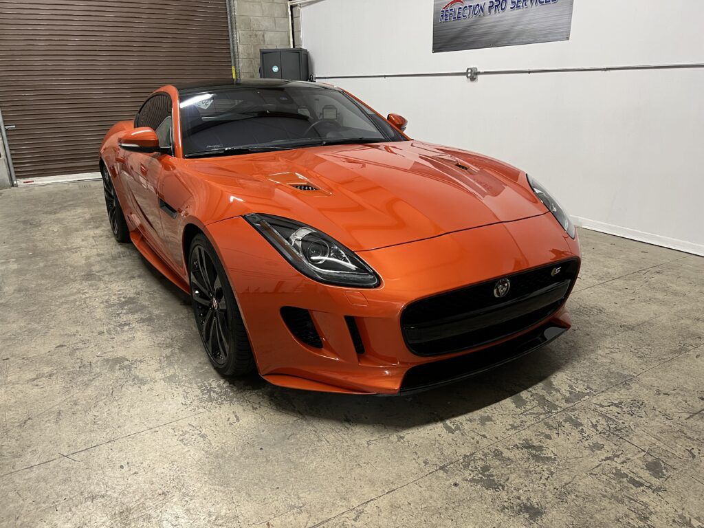 An orange jaguar f type is parked in a garage.