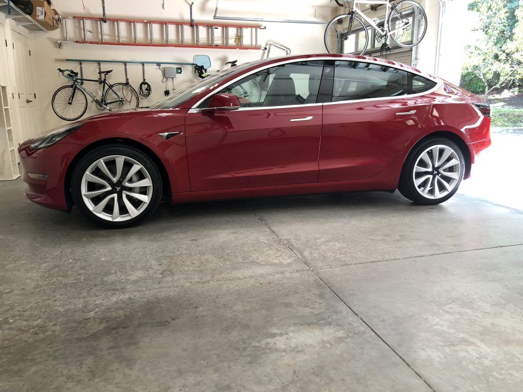 A red tesla model 3 is parked in a garage.