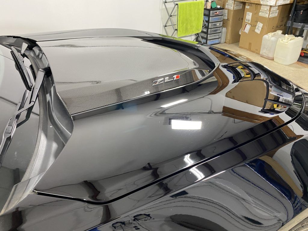 The hood of a black car is sitting in a garage.