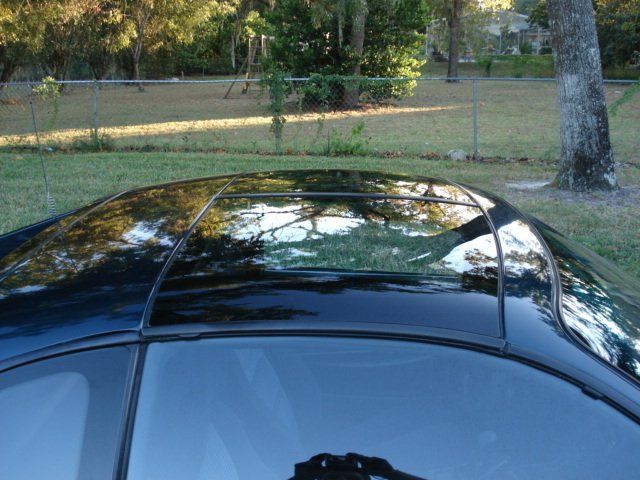 A black car is parked in a grassy area with trees in the background