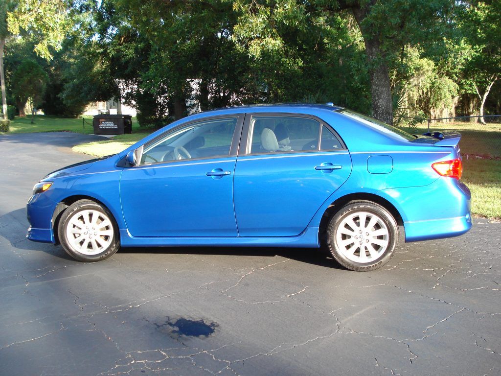 A blue car is parked in a driveway with trees in the background
