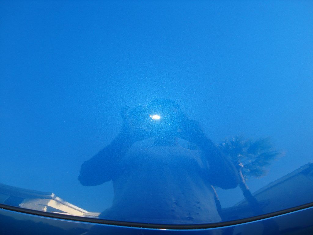 A person is taking a picture of themselves on the hood of a blue car.