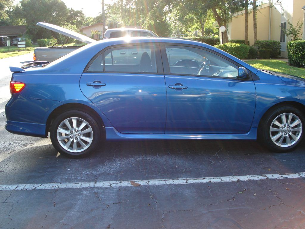 A blue car with the trunk open is parked in a parking lot