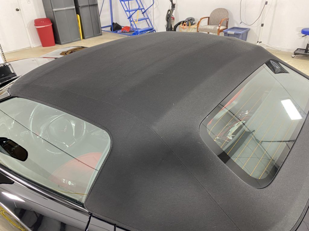 A black convertible car with a black roof is parked in a garage.