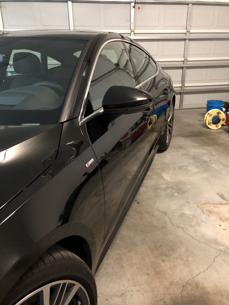 A black car is parked in a garage next to a garage door.