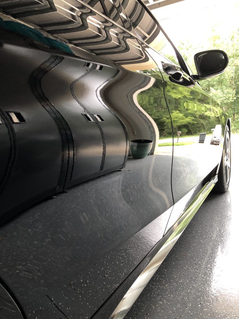 A black car is parked in a garage with trees in the background.