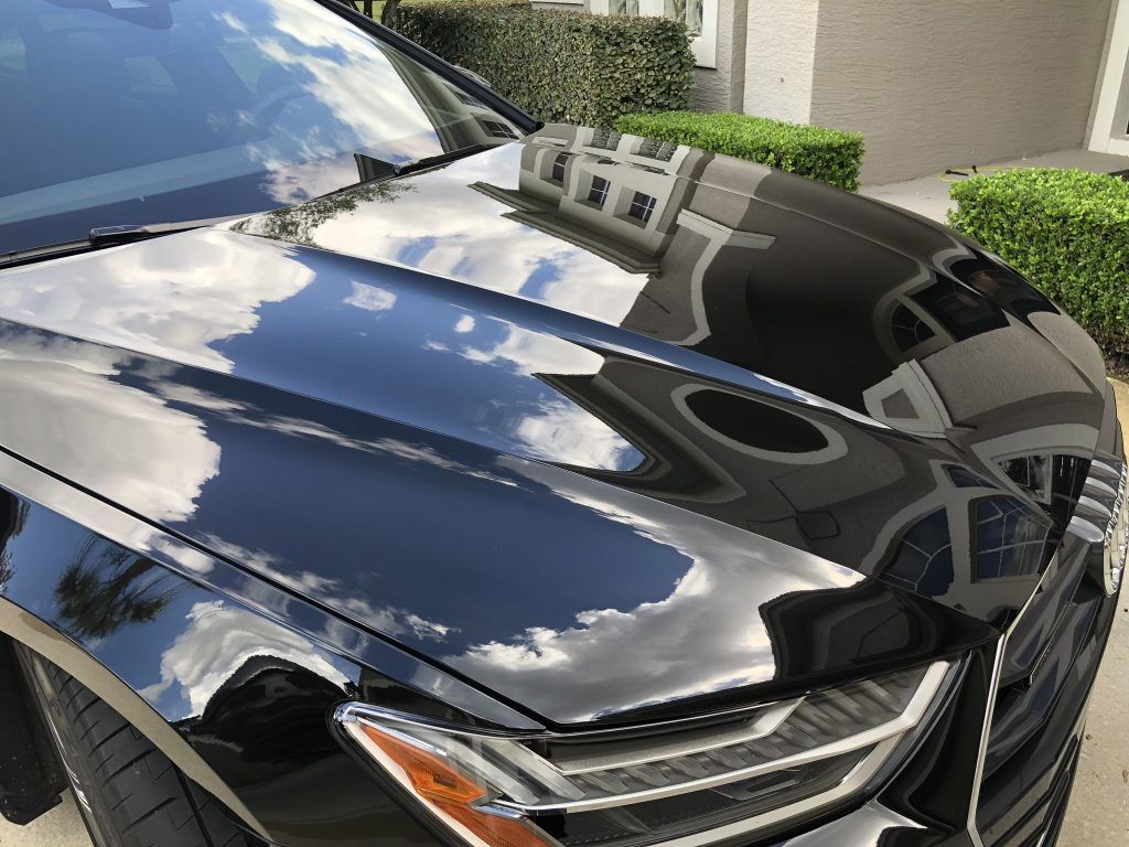 A black car is parked in a driveway in front of a house.
