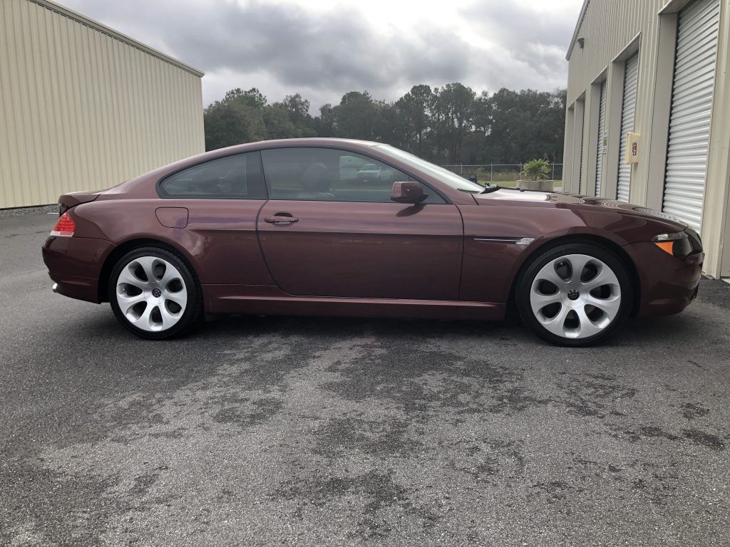 A burgundy bmw 6 series coupe is parked in front of a building.