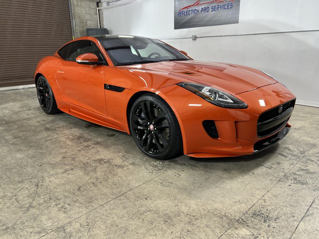An orange jaguar f type is parked in a garage.