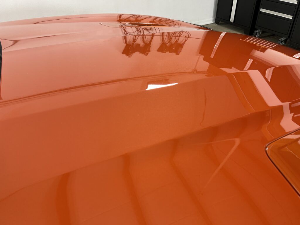 A close up of the hood of an orange car in a garage.