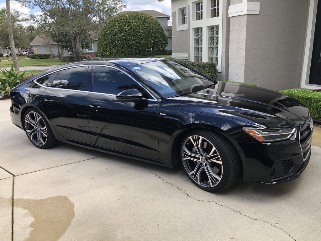 A black car is parked in a driveway in front of a house.