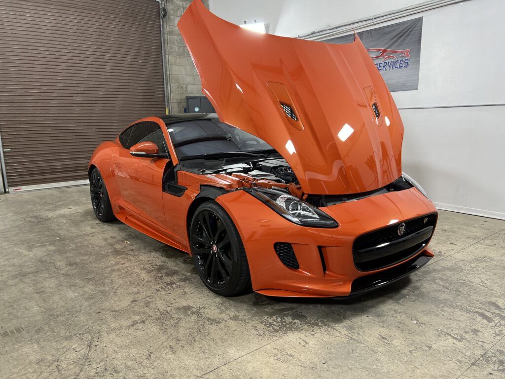 An orange sports car with the hood up is parked in a garage.