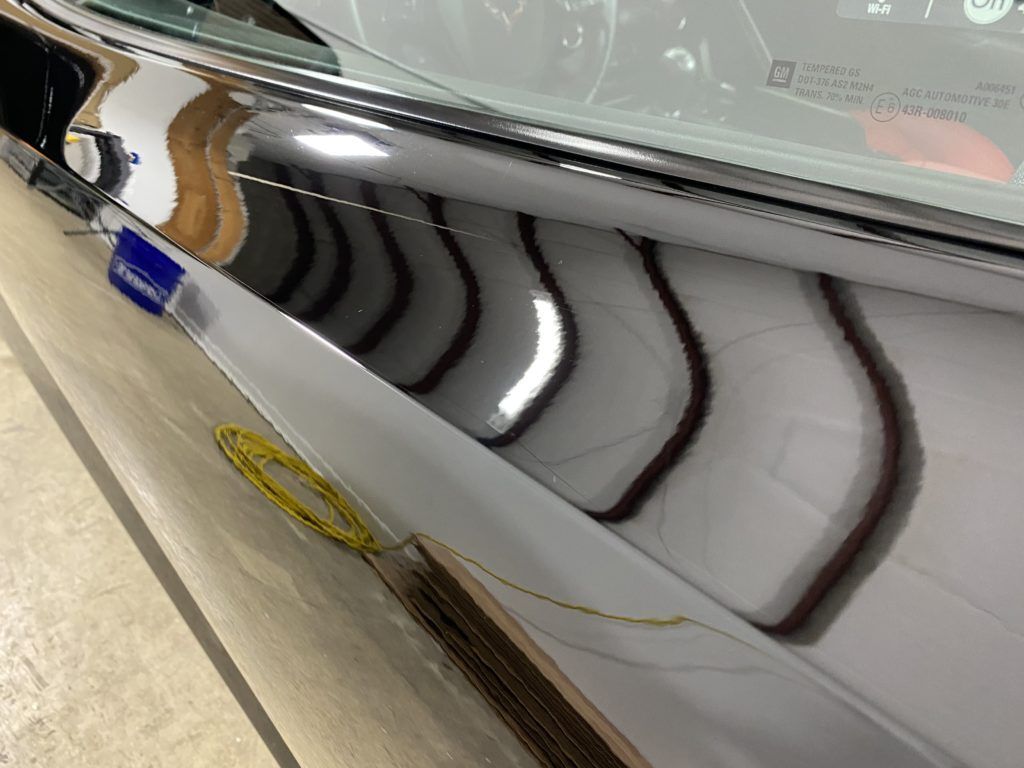A close up of a car 's side with a reflection of a building in the window.