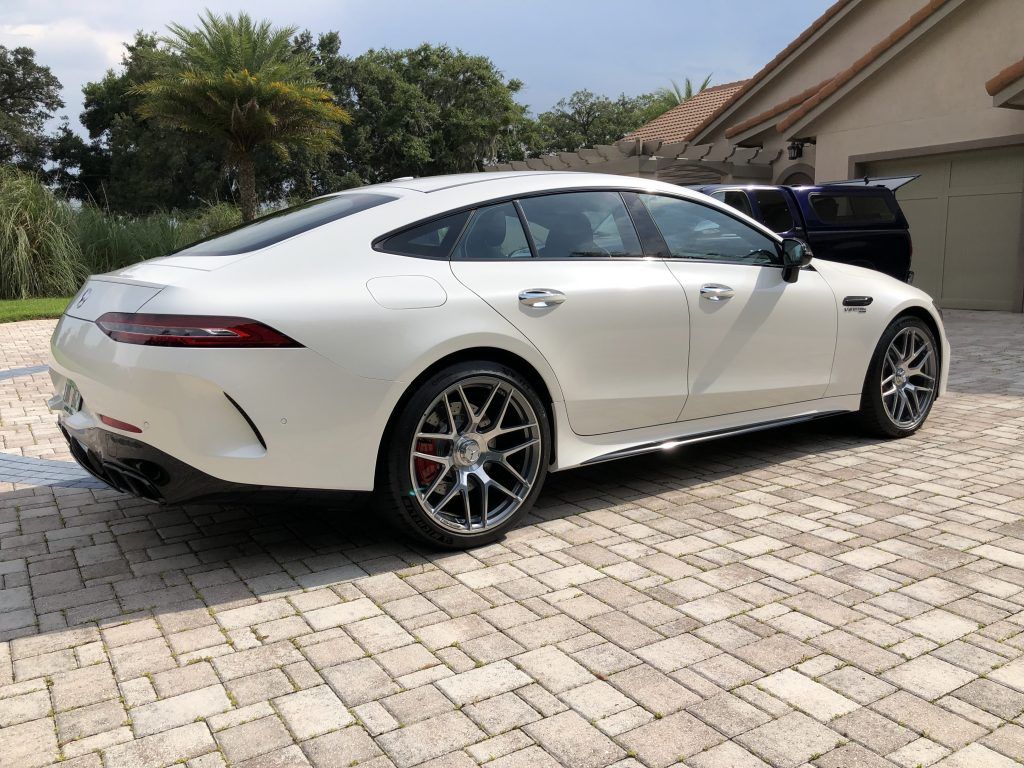 A white sports car is parked on a brick driveway in front of a house.