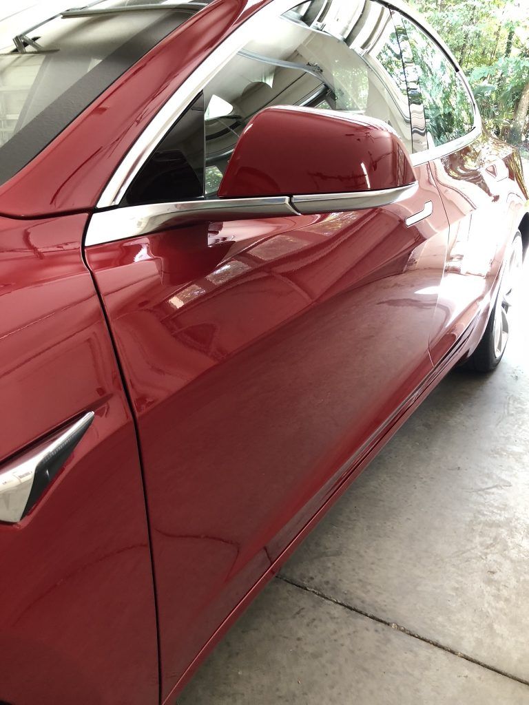 A red tesla model 3 is parked in a garage.