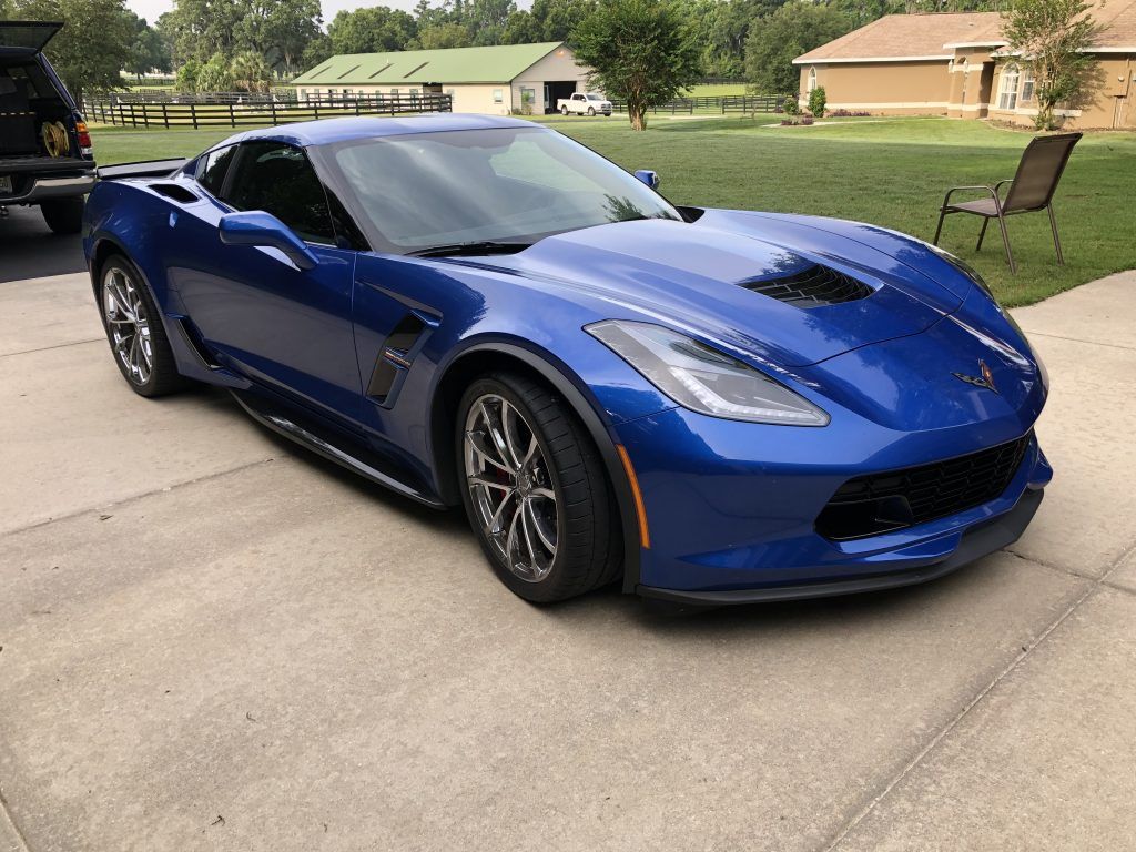 A blue corvette is parked in a driveway next to a house.