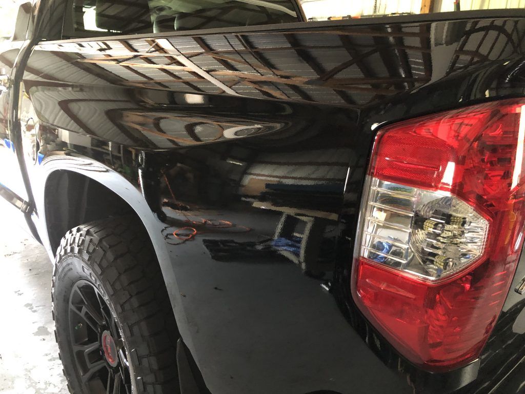 A black truck with a red tail light is parked in a garage.
