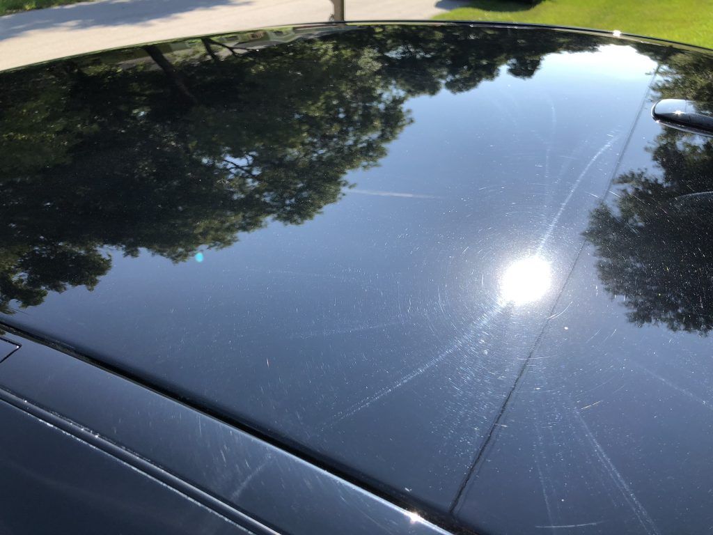 A close up of a black car 's roof with trees reflected in it