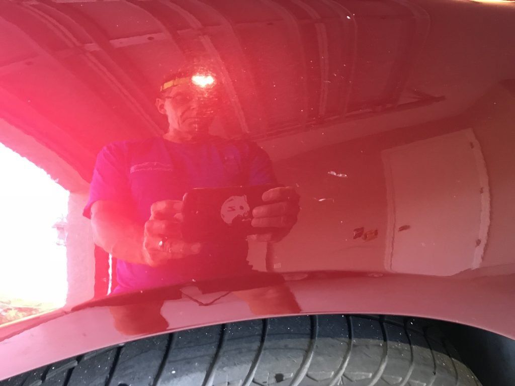 A man is taking a picture of himself in the hood of a red car.