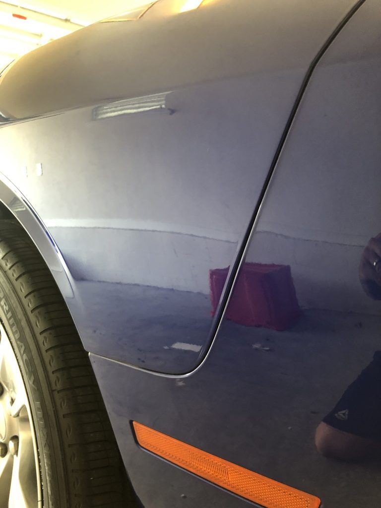 A blue car is parked in a garage with a reflection of a person in the door.