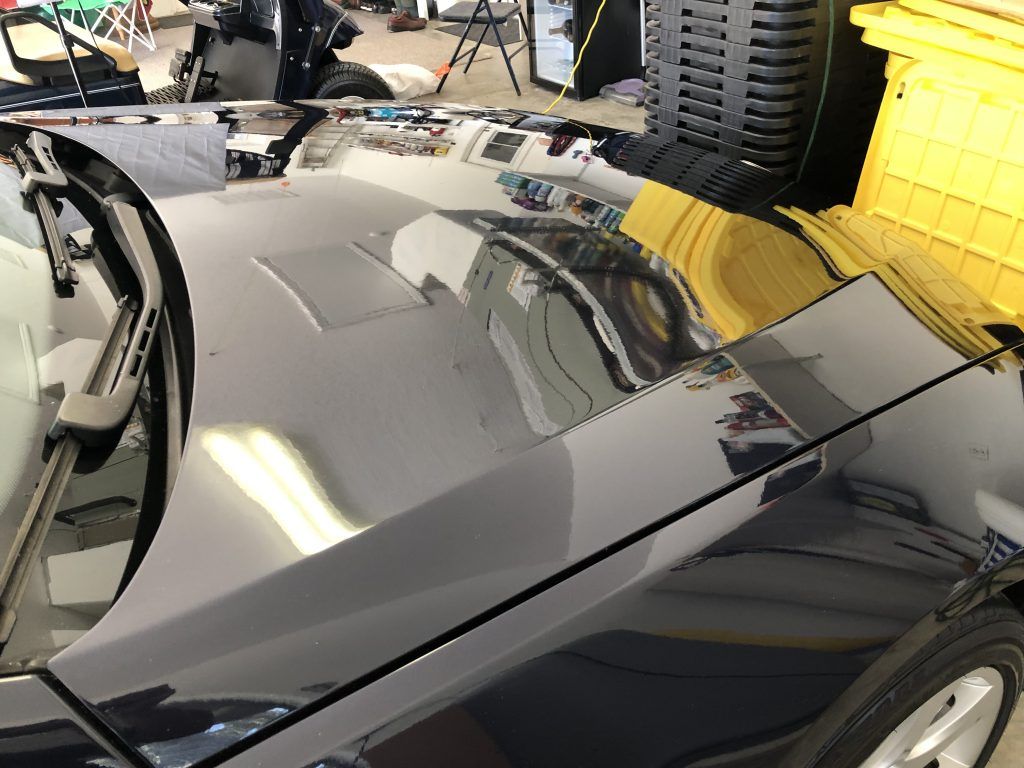 A black car is parked in a garage with the hood up.