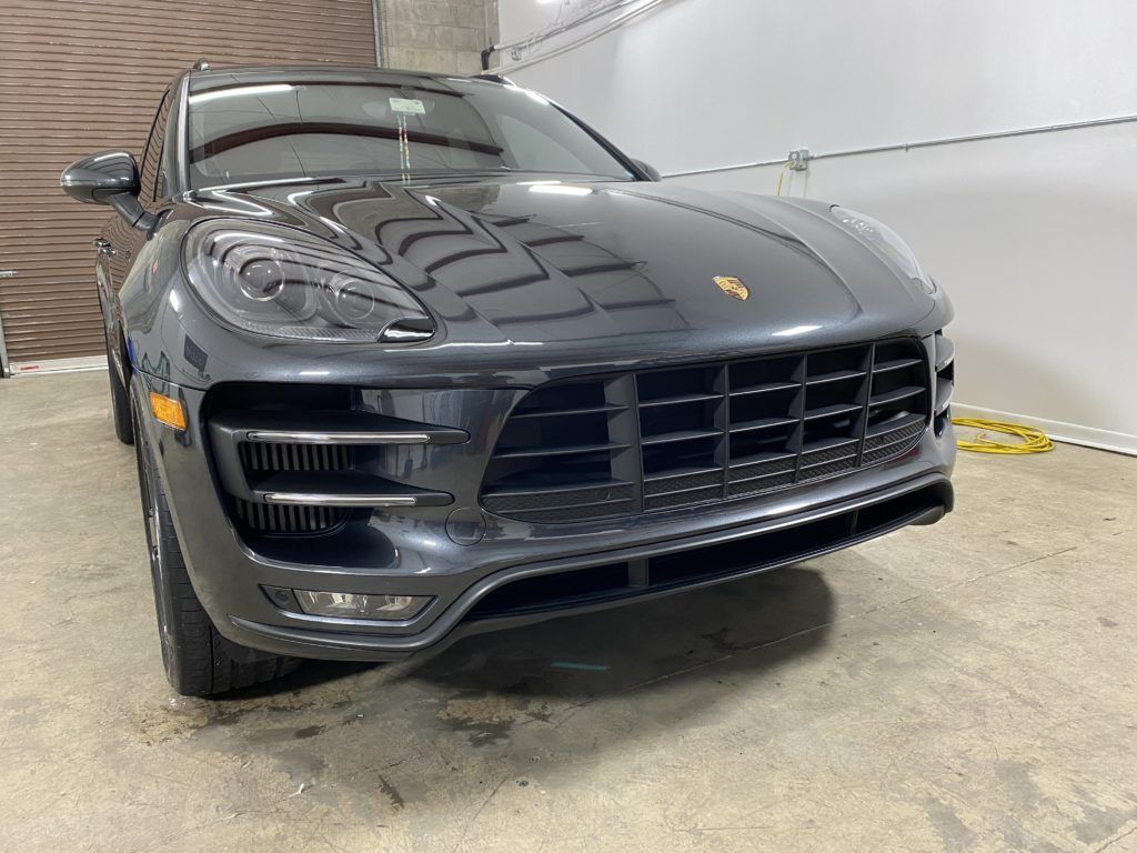 A gray porsche macan is parked in a garage next to a garage door.