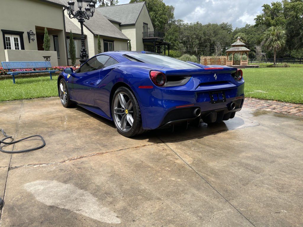 A blue ferrari 488 gtb is parked in a driveway in front of a house.