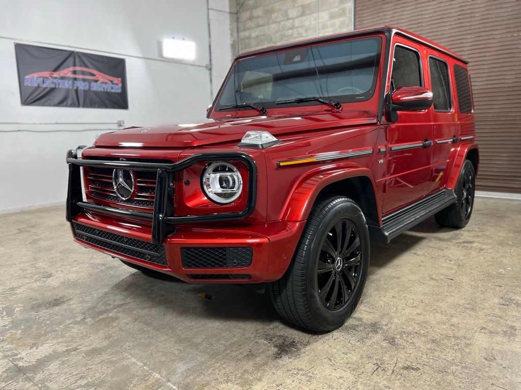 Red Mercedes-Benz G-Class SUV with black wheels parked in a garage with a banner.