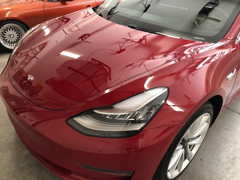 A red tesla model 3 is parked in a garage next to another car.