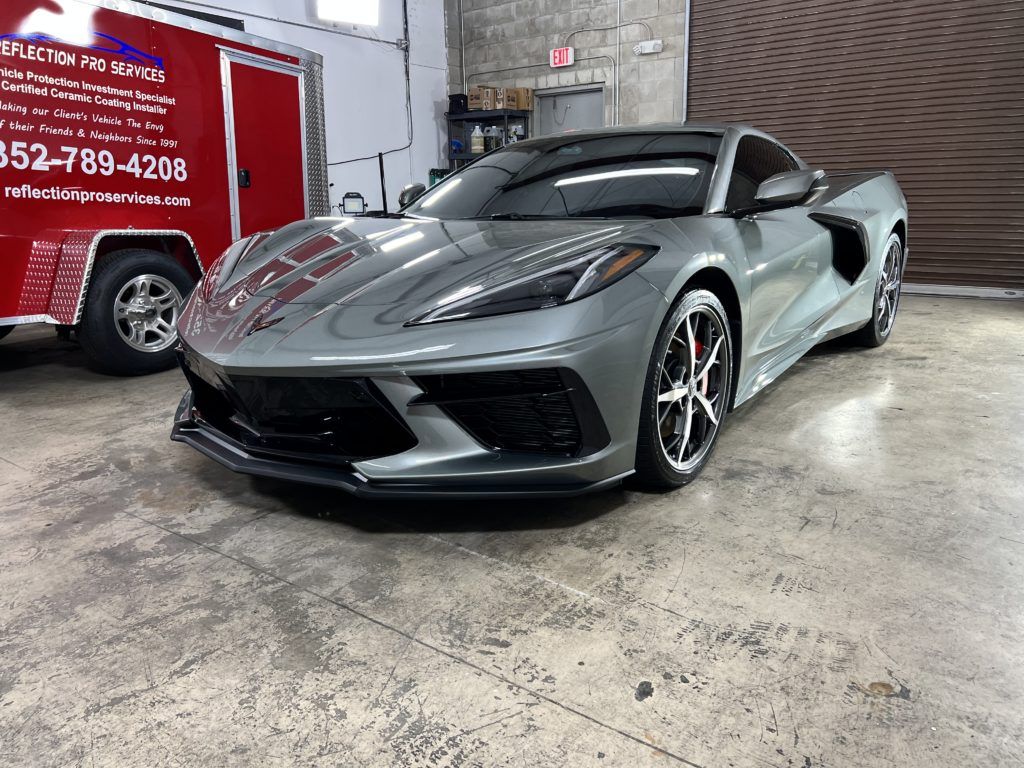 A gray sports car is parked in a garage next to a red trailer.