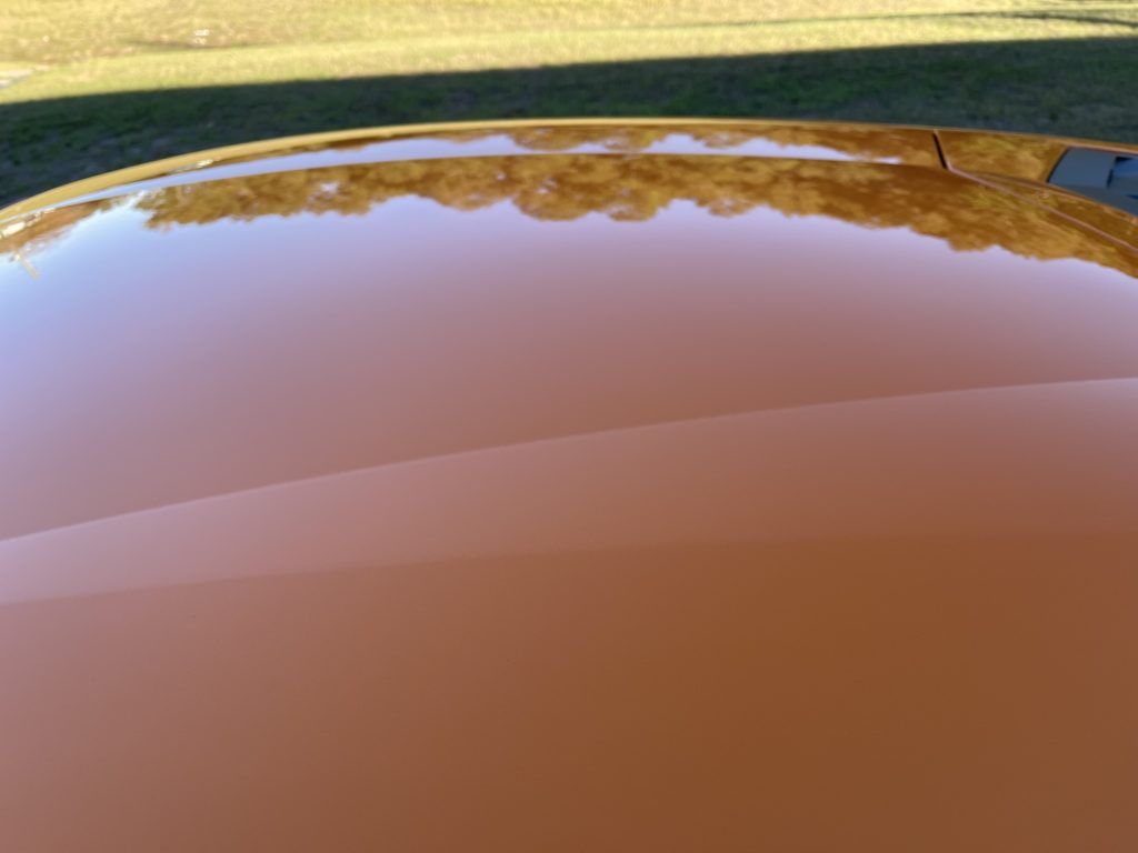 A close up of the hood of a car with trees reflected in it.