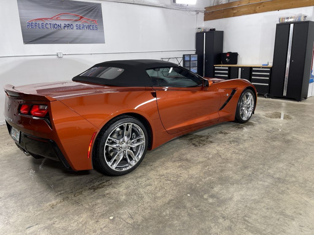 An orange convertible corvette is parked in a garage.