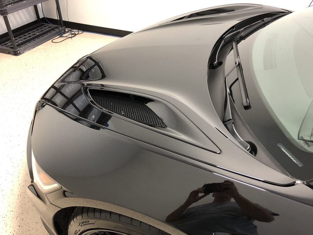 A black car is parked in a garage with the hood open.