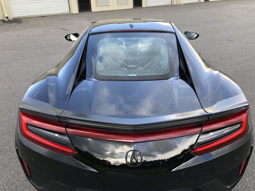 A black sports car with a red tail light is parked in a parking lot.