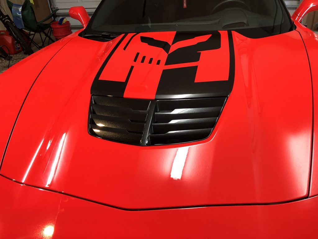 A red sports car with a black hood is parked in a garage.