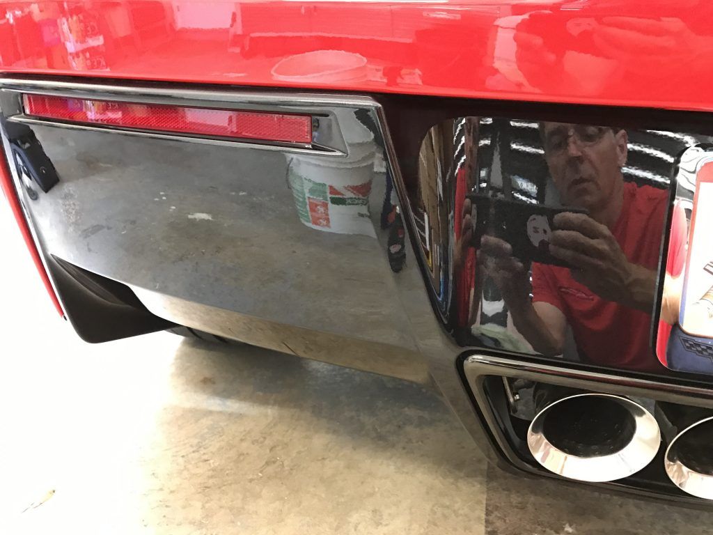 A man is taking a picture of his reflection in the bumper of a red car.