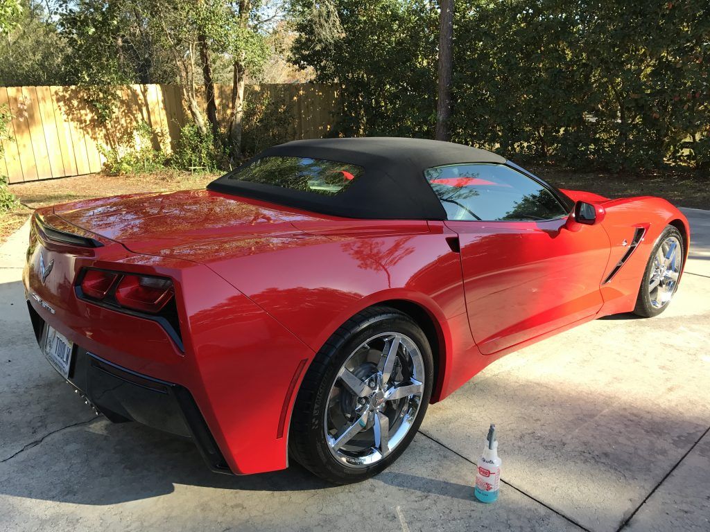 A red sports car with a black top is parked in a driveway.