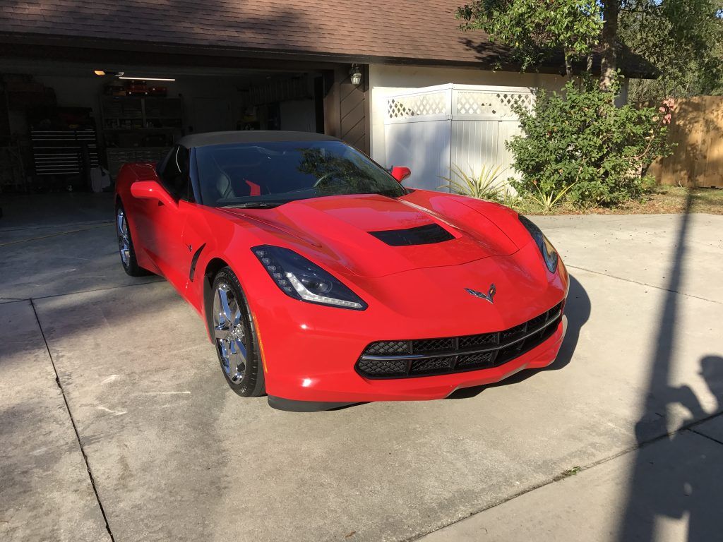 A red corvette is parked in a driveway in front of a garage.