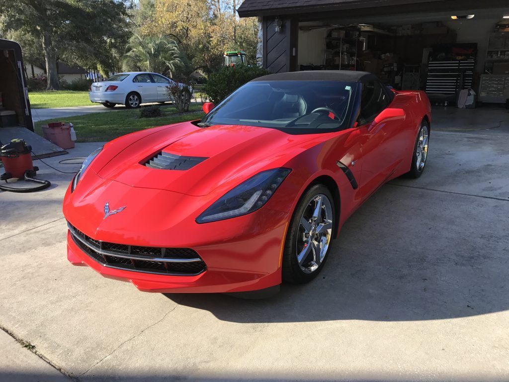 A red corvette is parked in a driveway in front of a garage.