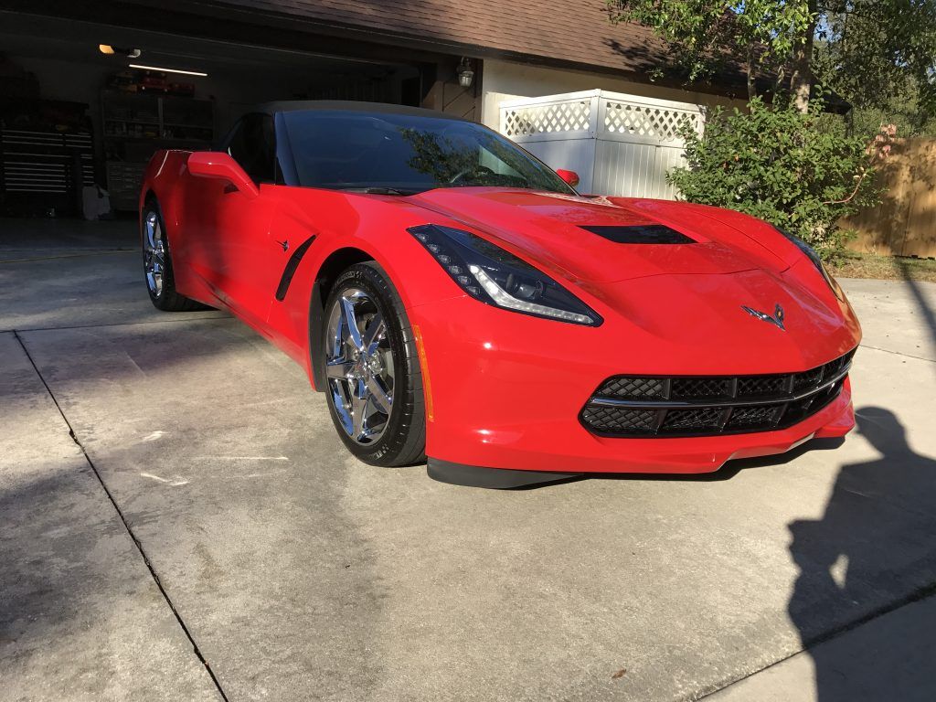 A red corvette is parked in a driveway in front of a garage.