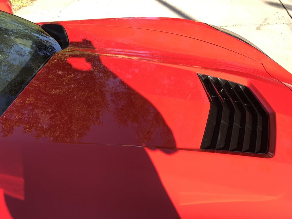 A close up of a red car hood with a black vent.