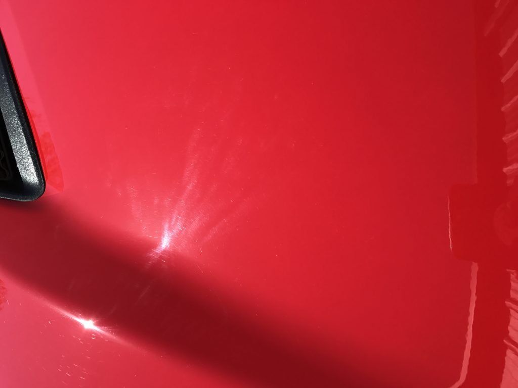 A close up of a red car hood with a black trim.