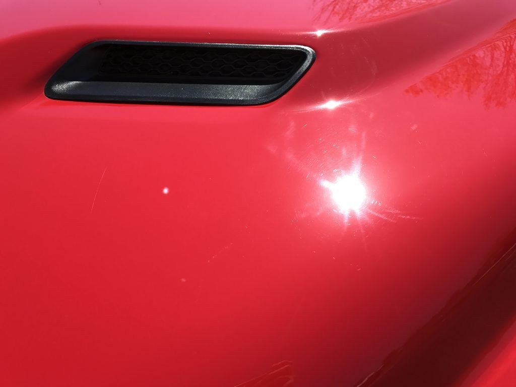 A close up of a red car hood with a black hood scoop.