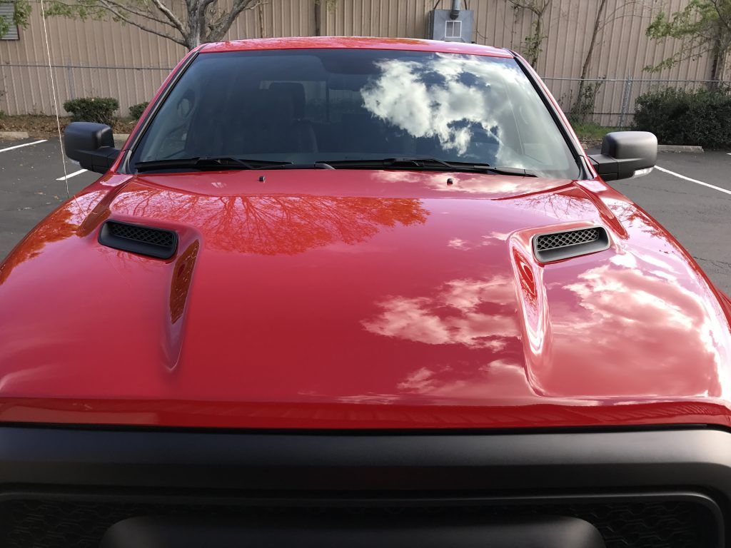 A red truck with a black hood is parked in a parking lot.