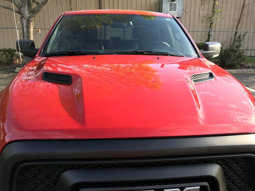 A red truck with a black hood is parked in a parking lot.