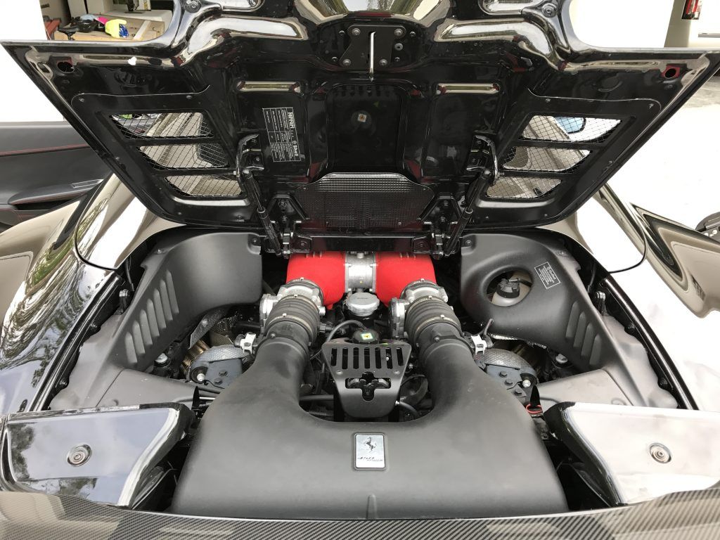 The engine of a ferrari 458 italia is shown with the hood open.