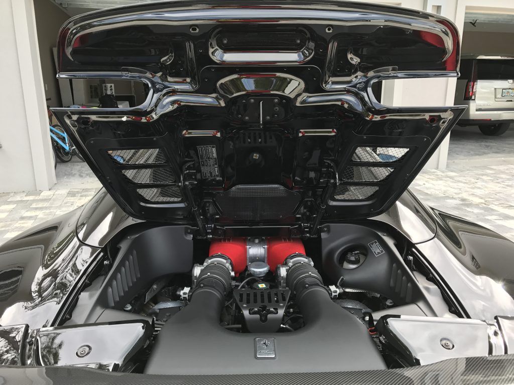 The hood of a black sports car is open and shows the engine.