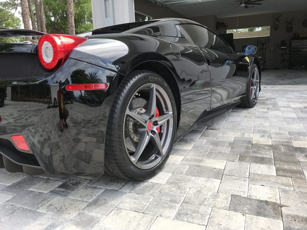 A black sports car is parked in a driveway next to a garage.